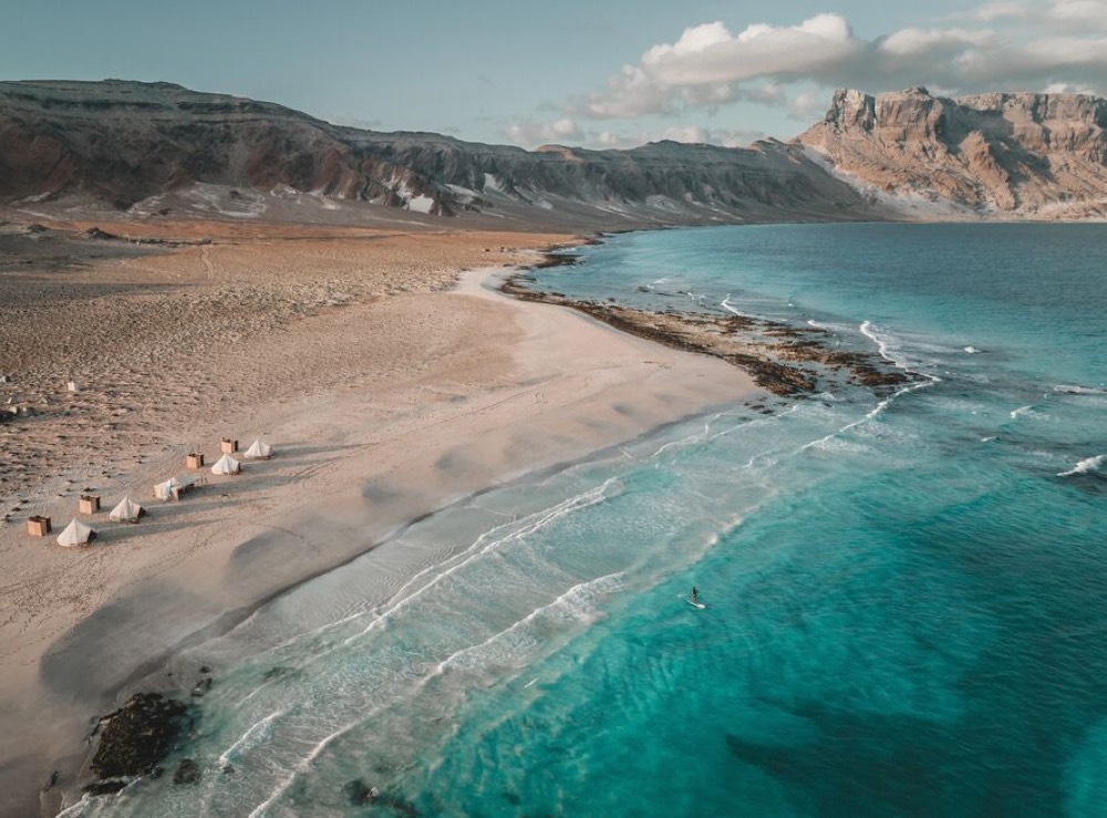 Tented camp above the surf, a paddler offshore, Socotra, Yemen
